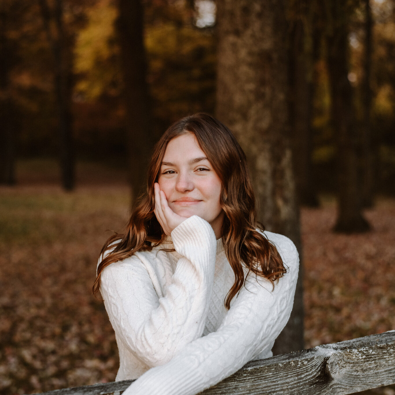 High school senior in Northeast Ohio posing in a park, leaning over a wooden fence during their senior photo session.